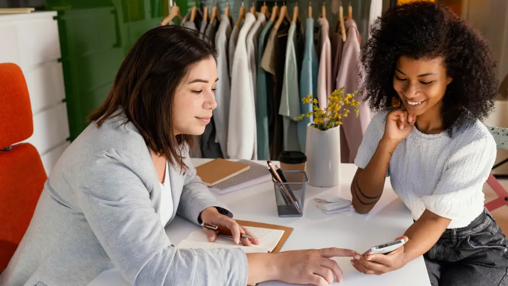 Duas mulheres em uma loja de roupas avaliando diferentes sistemas de gestão para loja de roupas em um celular.